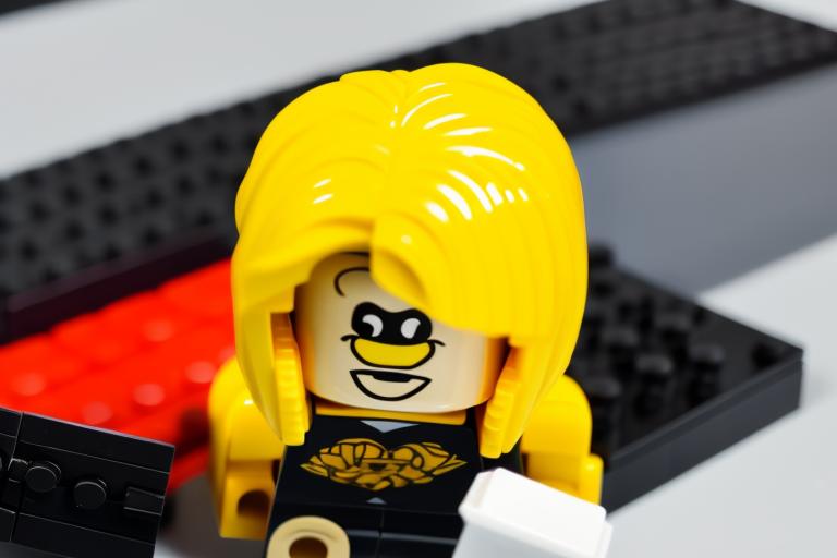 A female version of Pepper Roni, the main character of the Lego Island games, with orange-blonde hair, dressed in an orange shirt and a black suit. She is lying down on a Lego matras and bleeding Lego blood from a bullet shot in her belly.